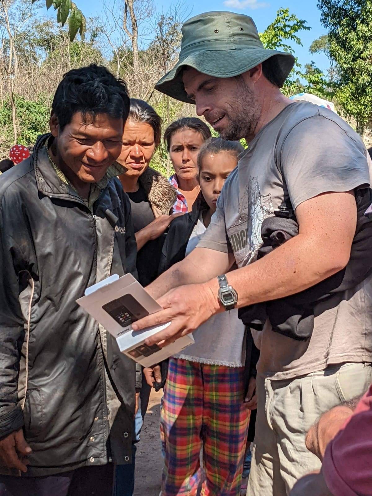 Man showing an audio device to three adults and a young person in Paraguay. They are standing outside.